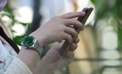 Obraz premium A woman sitting on a chair In the garden on her wrists are expensive luxury watches.