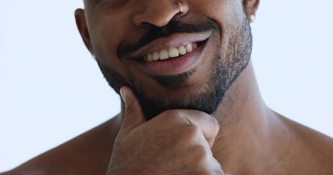 Smiling charming african american unshaven bearded young man with bristle touching beard advertising shaving or aftershave skin care product, barber shop grooming services concept. Close up view
