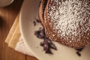 A view of delicious cocoa pancakes with dark chocolate and powdered sugar on a wooden table