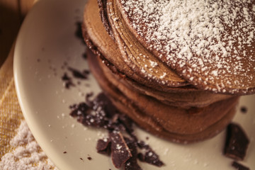 A view of delicious cocoa pancakes with dark chocolate and powdered sugar on a wooden table