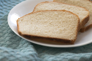 Sliced of freshly, homemade white bread on a white plate with a textured blue cloth background.