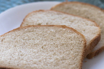 Sliced of freshly, homemade white bread on a white plate with a textured blue cloth background.