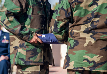 American Flag in the process of being folded by soldiers dressed in camouflage fatigues. Military...