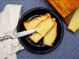 Fresh yellow cornbread out of the oven sliced and served with butter on a knife sitting on a navy blue plate and blue tablecloth.