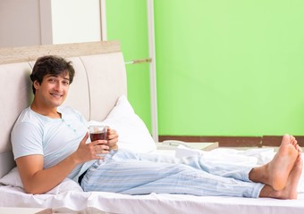 Young handsome man drinking coffee in the bed