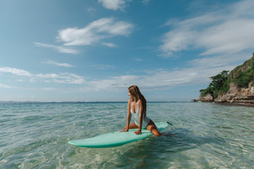 Girl sitting on a surf board in the ocean and looking for the waves. Happy girl in bikini have fun before surfing Surfer lie on surf board