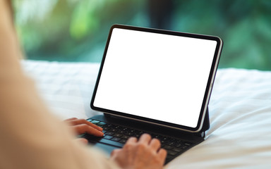 Mockup image of a woman using and typing on tablet pc with blank white desktop screen as computer pc while lying down on a cozy white bed at home