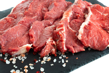 Beef. Fresh raw beef steaks on a black slate plate. Raw ribeye steaks on a slate plate with salt and pepper. Steaks with spices on a black slate board.