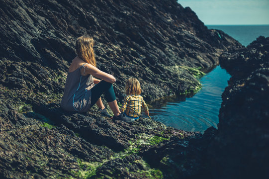 Mother and preschooler relaxing near rock pool by the sea