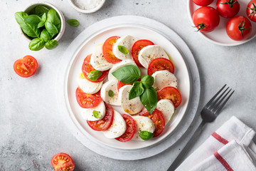 Italian caprese salad with sliced tomatoes, mozzarella, basil, olive oil on a light background. Top...