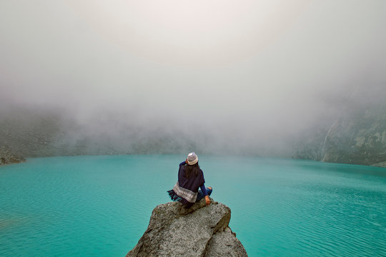Woman sitting on a stone looking at the crystal clear waters of the "lagoon 69" in Huaraz Peru.