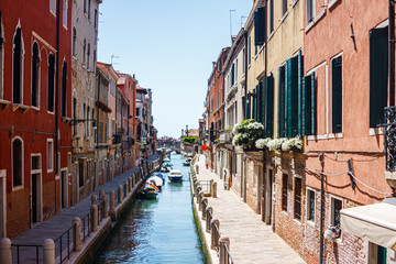Cityscape with ancient buildings with flowers on their balconies on both sides of the canal in Venice, Italy.