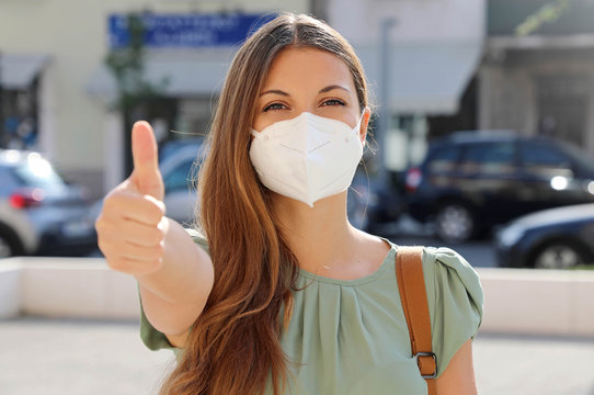 COVID-19 Positive young woman wearing protective mask KN95 FFP2 avoiding Coronavirus disease 2019 showing thumbs up in city street
