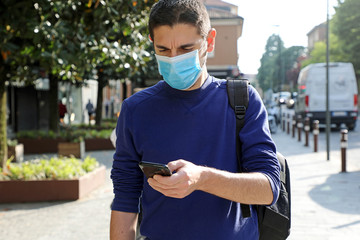 COVID-19 Pandemic Coronavirus Worried Young Man Wearing Surgical Mask Using Smart Phone App in City...