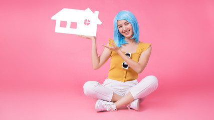 Young  Asian woman holding paper home cutout on light blue banner background for real estate concept.copy space isolated on pink banner background.
