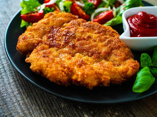 Pork chop with boiled potatoes and vegetable salad on wooden background