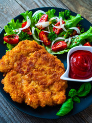 Pork chop with boiled potatoes and vegetable salad on wooden background