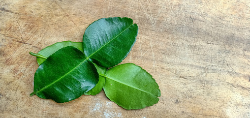 Two kaffir lime leaves, one upside down and the other face up on the wood floor.