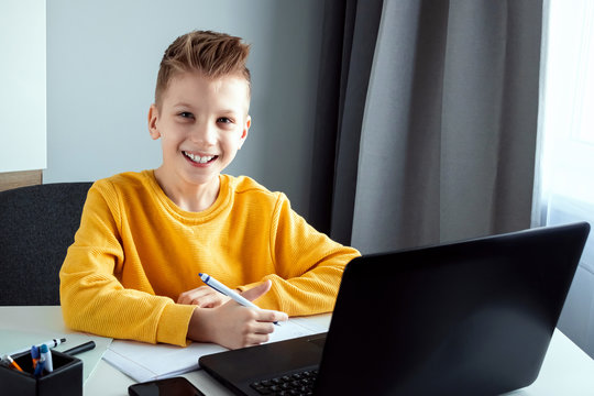 A child, a boy in a yellow jacket, is sitting at a table at home looking at a laptop, online learning, distance learning at home via the Internet. Technology, school, knowledge. Copy space.