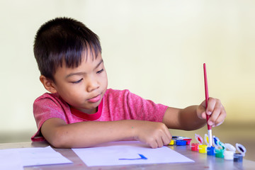 Portrait image of 5 yeas old child boy. Asian student drawing and painting colours on the paper in the room. Study​ from​ home, social​ Distancing, Kid and education concept.