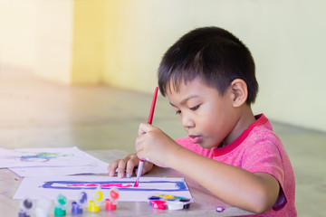 Portrait image of 5 yeas old child boy. Asian student drawing and painting colours on the paper in...