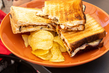 Aperitif before lunch in a bar in the city of Bari, in southern Italy. Chips and a toast with mozzarella, grilled eggplant and tomato on a brown plate.