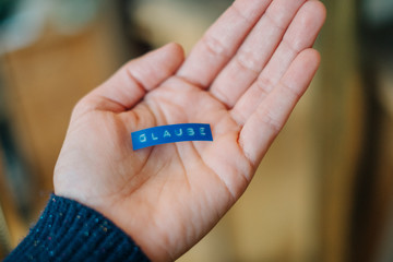 Eine Person die ein blaues Etikett mit dem geschriebenen Wort Glaube in der Hand hält