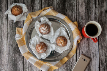 Muffins on a metal plate and coffee in a red ceramic mug, next to a smartphone stand on a wooden background. Flat lay. Top view