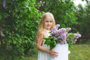 Small and beautiful girl child cute and happy with lilac flowers in her hands in nature