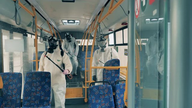 Men in hazmats sanitize city bus to kill virus.