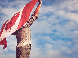 Attractive man holding Canadian Flag on blue sky background on a clear, sunny day. View from the...