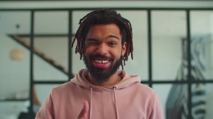 Cheerful carefree handsome african american young man with dreadlocks looking with radiant toothy smile, gesturing thumbs up happily, expressing positivity, joy and excitement indoors.