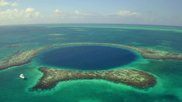 Aerial view of yacht near marine sinkhole against sky, drone panning from left to right over sea on sunny day - Great Blue Hole, Belize