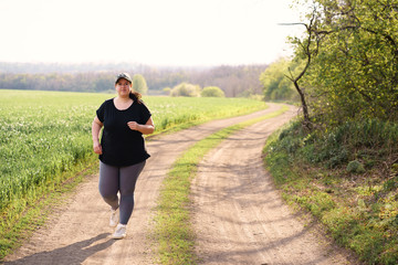 Young overweight woman running in nature. Female jogger doing morning physical training. Outdoor...