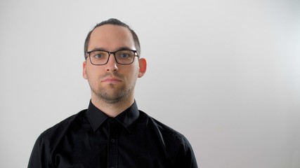 Obraz premium Portrait serious face of young man in glasses with black hair close up. Cute man looks positive. Bearded handsome man in a black shirt looking to camera. Confident attractive close up confidence. 