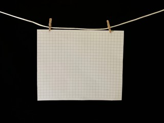 A piece of paper hanging on a rope, on a black background. A sheet of notebook attached to the...