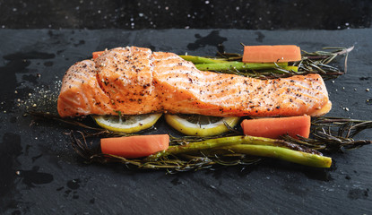 Grilled Salmon baked fillet steak, with lemon, Asparagus, Rosemary and Carrot on black stone plate