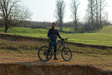 Fototapeta na wymiar Cyclist in shorts and jersey on a modern carbon hardtail bike with an air suspension fork standing on a cliff against the background of fresh green spring forest