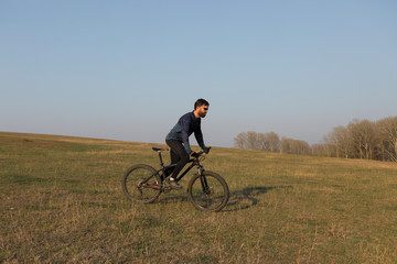 Obraz premium Cyclist in shorts and jersey on a modern carbon hardtail bike with an air suspension fork standing on a cliff against the background of fresh green spring forest