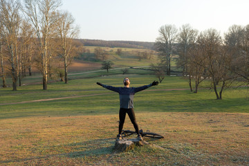 Cyclist in shorts and jersey on a modern carbon hardtail bike with an air suspension fork standing on a cliff against the background of fresh green spring forest