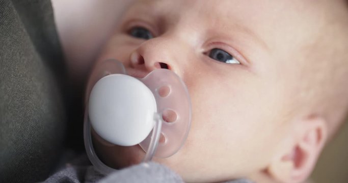 Closeup shot of a newborn baby girl sucking on a pacifier in the arms of her mother.
