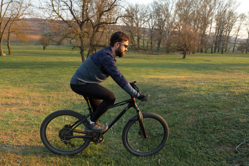 Cyclist in shorts and jersey on a modern carbon hardtail bike with an air suspension fork standing on a cliff against the background of fresh green spring forest