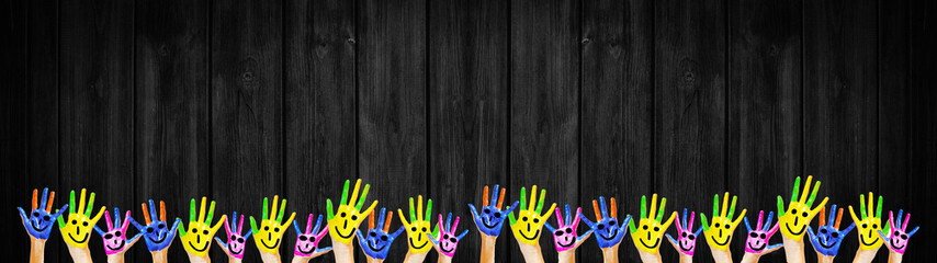 School background banner panorama - Many brightly painted children's Hands, isolated on black wooden wall texture, with space for text