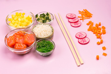 Set of raw vegetables, red fish, rice, soy sauce in glass bowls. Hawaiian dish. Bamboo chopsticks