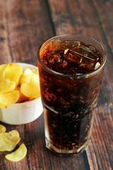 A glass of iced cola with potato chips on wooden table. Soft drinks and potato crisps.