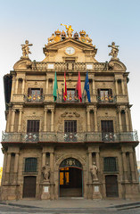 Pamplona, Spain - 10/10/2019: Empty city hall with flags in Pamplona. Famous square in centre of Pamplona. Exterior of ancient medieval town hall. Clock and sculptures in city hall early in morning.