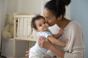 Loving young african American mother hold little newborn infant child kiss enjoying moment at home...
