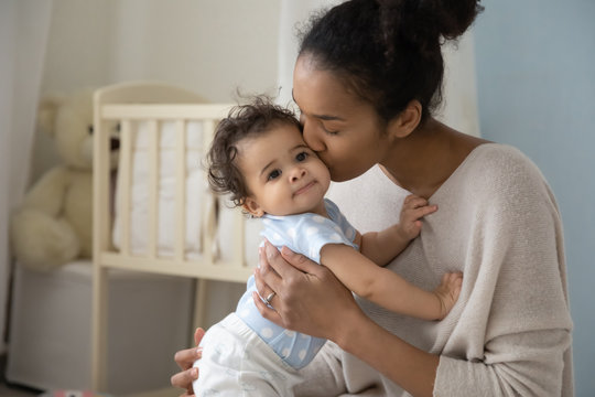 Loving young african American mother hold little newborn infant child kiss enjoying moment at home together, caring biracial mom embrace cuddle small baby toddler, maternity, childcare concept