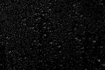 Drops of water flow down the surface of the clear glass on a black background.	