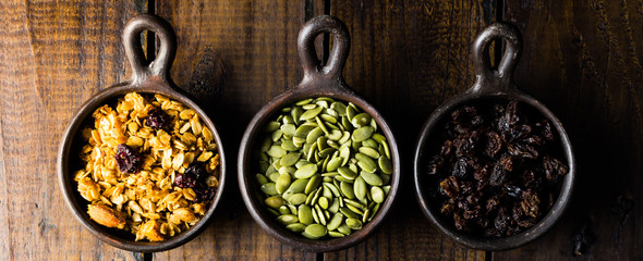 Variety of nuts, seeds and granola in a clay pots with a beautiful wooden rustic background. Healthy concept. Vegan Concept. Copy space. Top view